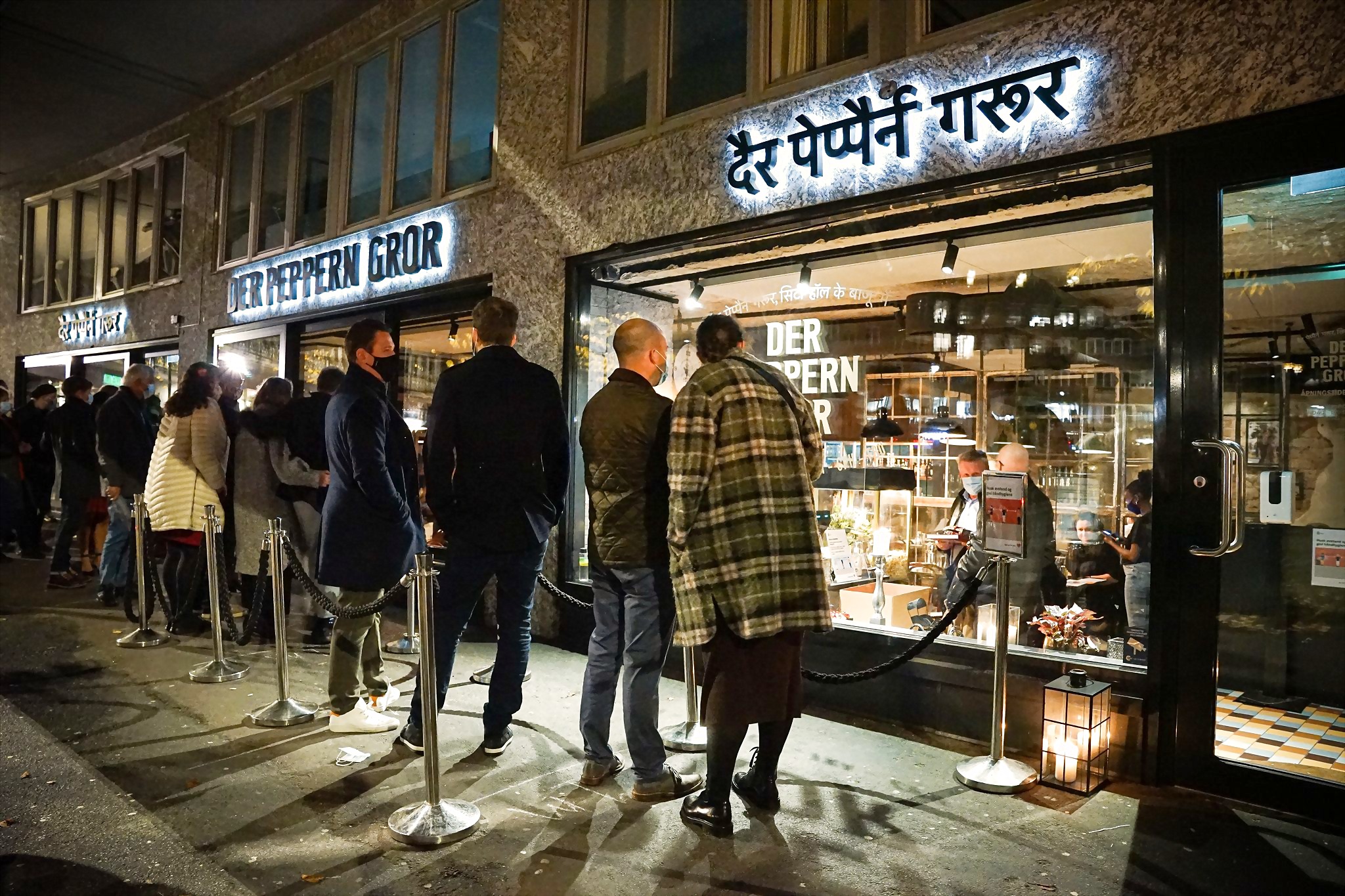 Der Peppern Gror på Rådhusplassen en vinterkveld — opplyst skilt, neon på devanagari og kø av gjester i varmt lys